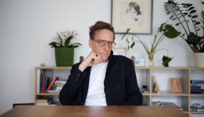Portrait von Kay Voges an einem Holztisch vor einem Regal mit Pflanzen